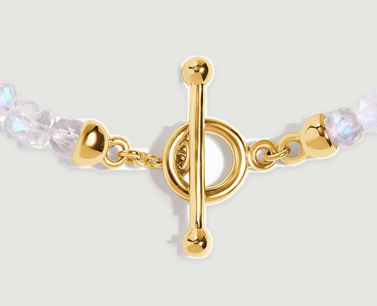 A yellow gold bar crosses its round clasp beside small links and shimmering moonstone beads.