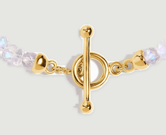 A yellow gold bar crosses its round clasp beside small links and shimmering moonstone beads.
