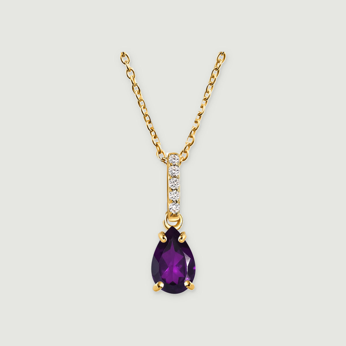 A yellow gold vermeil chain leads to a five-stone bail and a purple pear-shaped pendant centered on a light grey surface.