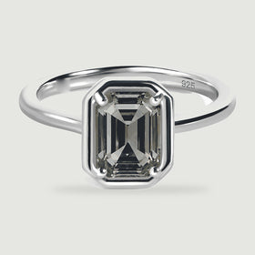 A grey emerald-cut stone shows dark stepped facets within a polished silver ring.