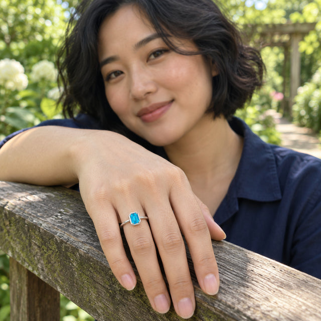 A woman in a navy shirt wears a blue-stone silver ring while resting her hand on a wooden garden railing.