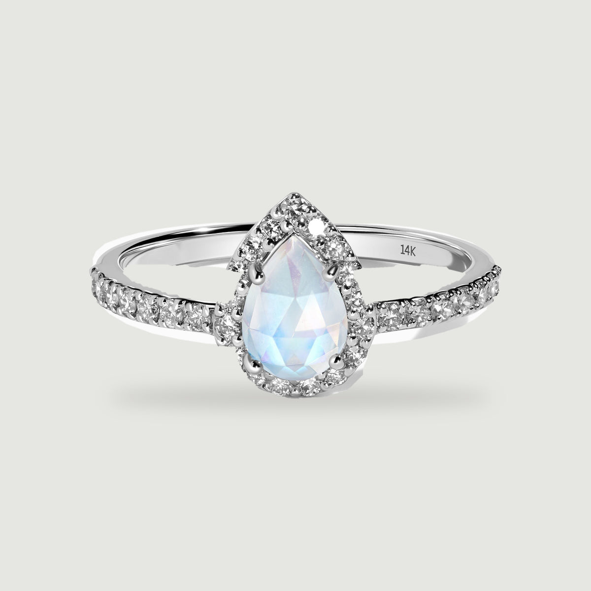 A white gold ring with a pear-shaped moonstone, a diamond halo and diamond-set shoulders on a pale grey surface.