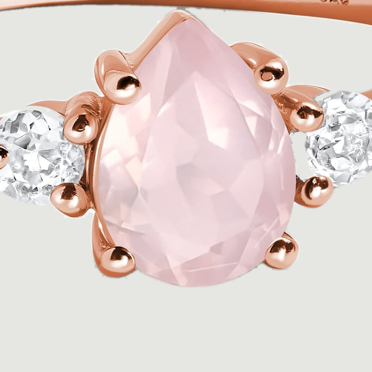 A close view shows the faceted pink pear-shaped center stone between two clear round stones in rose gold prongs.