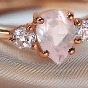 A close view of the ring on textured fabric reveals the pink gemstone facets and rounded rose gold prongs.