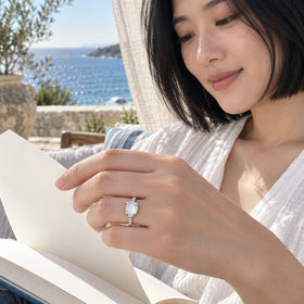 A woman with a black bob wears the silver moonstone ring while holding an open book beside a sea-facing window.