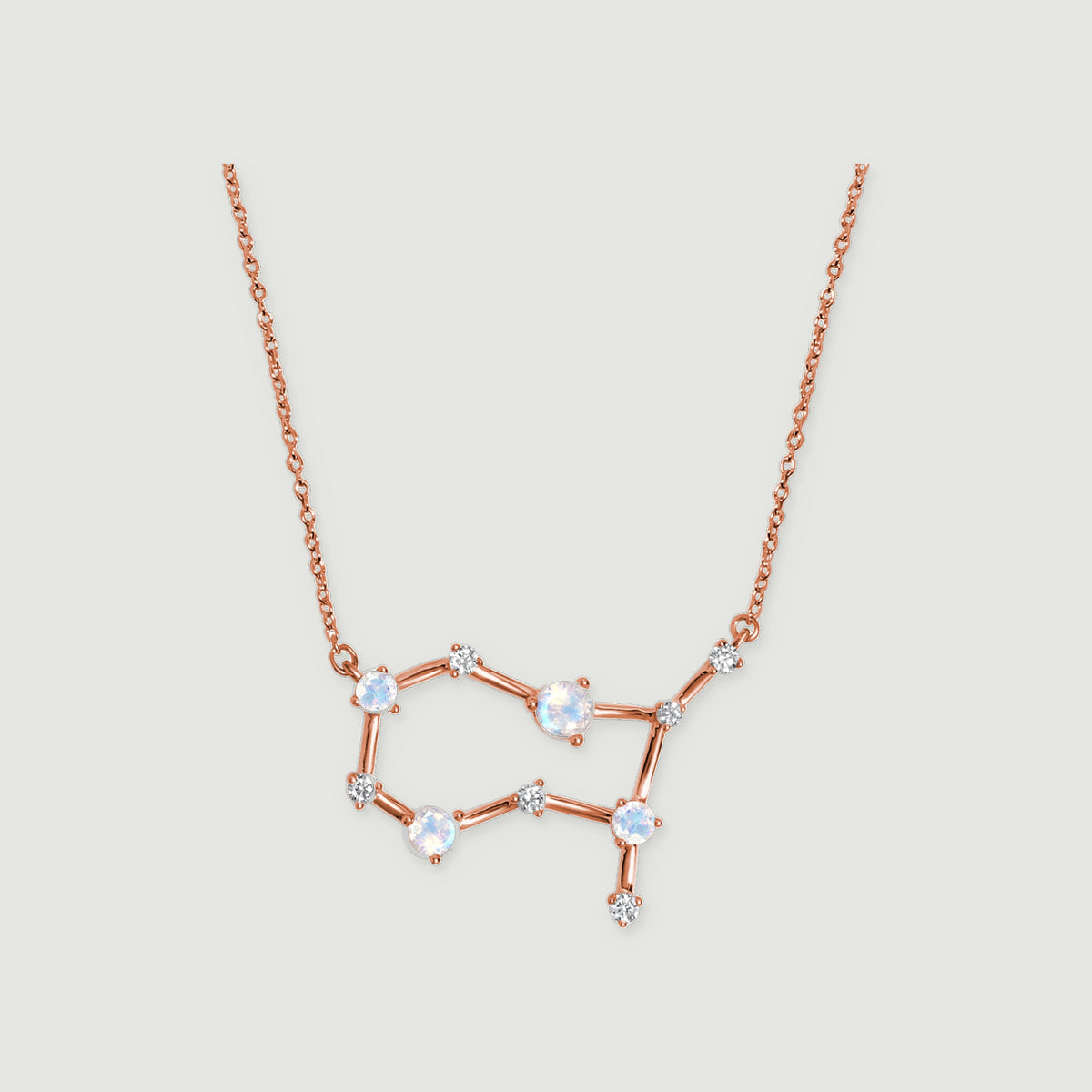 A rose gold necklace with four round moonstones and small clear stones rests against a pale gray background.