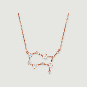 A rose gold necklace with four round moonstones and small clear stones rests against a pale gray background.