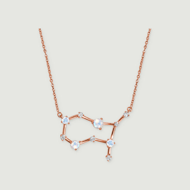 A rose gold necklace with four round moonstones and small clear stones rests against a pale gray background.