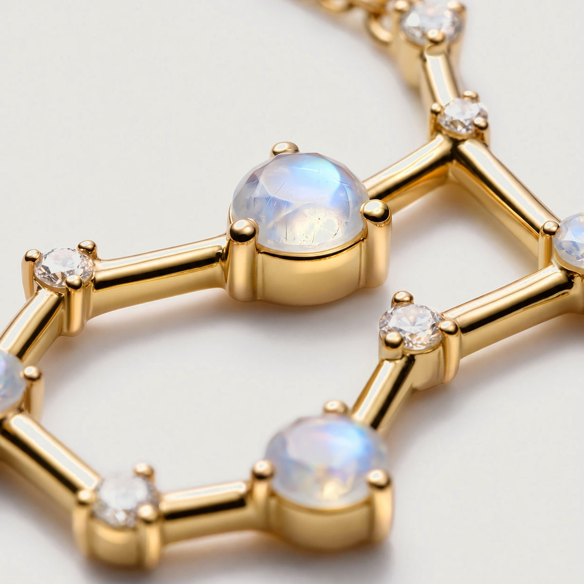 A close-up shows a blue-flashing moonstone held by rounded yellow gold prongs beside clear stones.