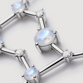 An angled close-up reveals the facets of a pale moonstone and smooth silver bars beside small clear stones.