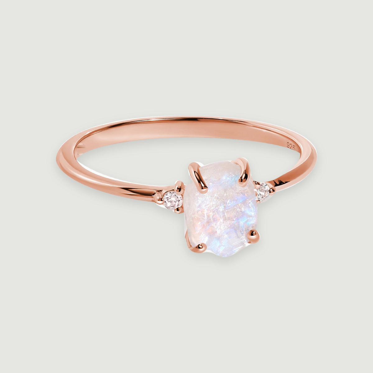 A rose gold vermeil band curves around an irregular moonstone with pale blue reflections and a white zircon on each side.