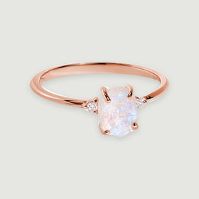 A rose gold vermeil band curves around an irregular moonstone with pale blue reflections and a white zircon on each side.