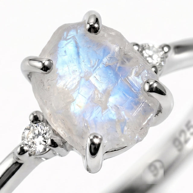 A close view reveals blue reflections inside the rough moonstone, silver prongs, and a round white zircon.