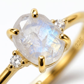 The textured moonstone and a faceted white zircon are held by polished yellow gold vermeil prongs in a tight detail view.