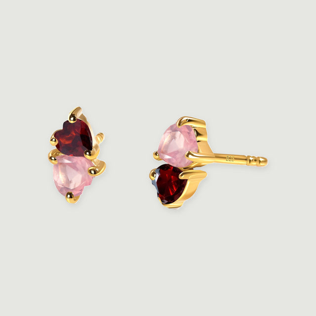 Yellow gold tone prongs frame pink rose quartz and red garnet hearts in a pair of stud earrings.