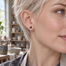 A woman with a short platinum blonde hairstyle wears a silver tone pink and red heart stud in a pottery studio.