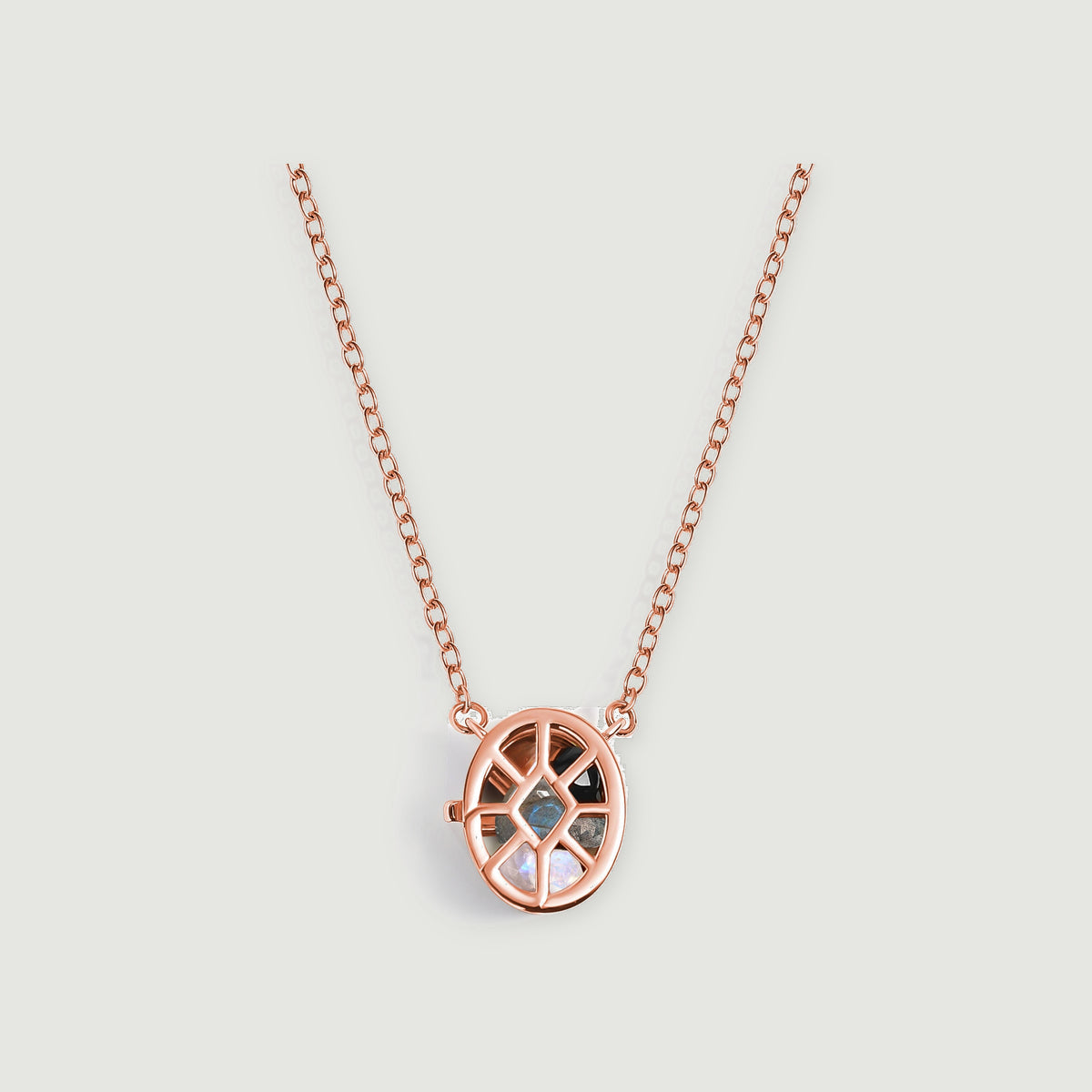 A rose gold oval cage pendant containing black, gray, and pearly gemstones hangs from a fine chain on a pale gray background.