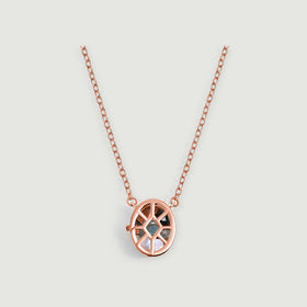 A rose gold oval cage pendant containing black, gray, and pearly gemstones hangs from a fine chain on a pale gray background.