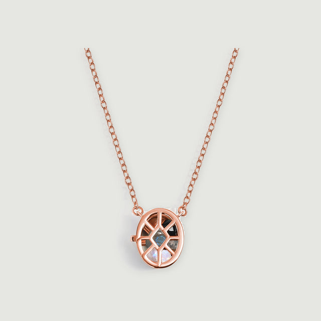 A rose gold oval cage pendant containing black, gray, and pearly gemstones hangs from a fine chain on a pale gray background.