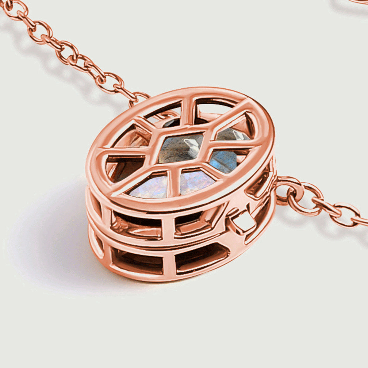 The rose gold locket rests at an angle, showing its raised cage and openings along the side.