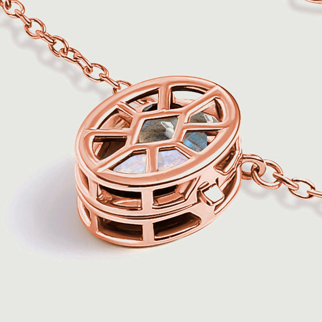 The rose gold locket rests at an angle, showing its raised cage and openings along the side.