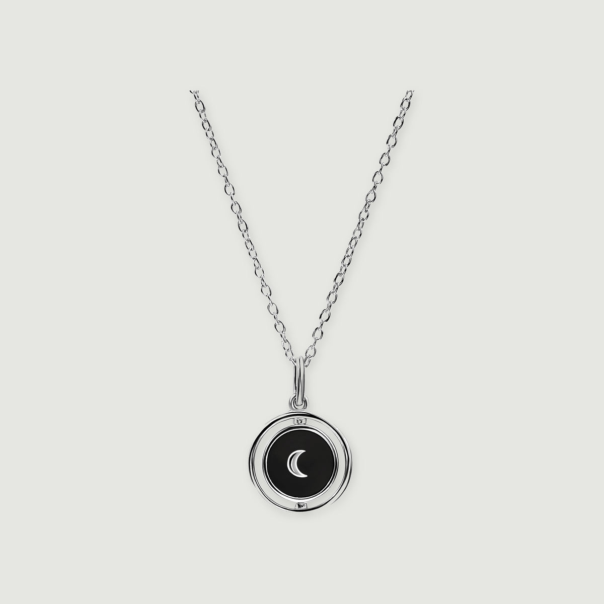 A sterling silver necklace shows a black circular pendant with a crescent inside an open polished ring.