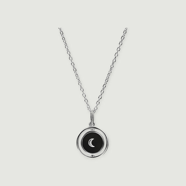 A sterling silver necklace shows a black circular pendant with a crescent inside an open polished ring.