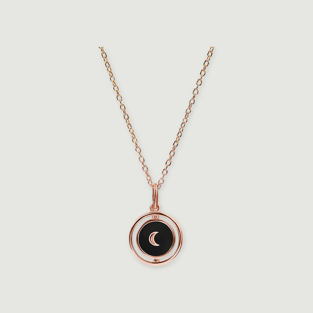A rose gold vermeil necklace has a glossy black pendant with a matching crescent and circular surround.