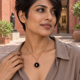 A woman with short dark hair wears the rose gold crescent necklace with a taupe blouse in a brick courtyard.