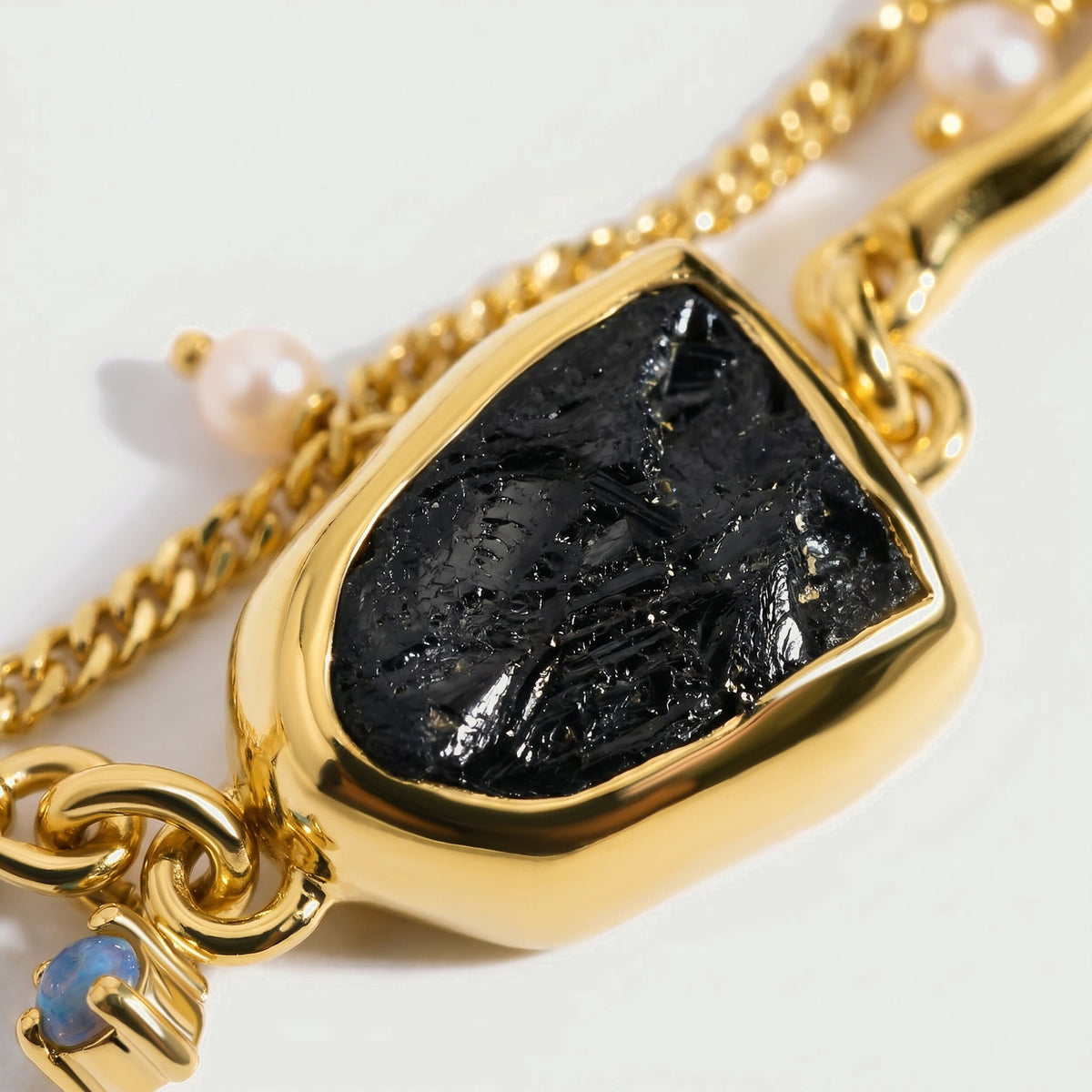 A close view shows the ridged black stone in a polished yellow gold setting beside a pearl and a pale blue accent.