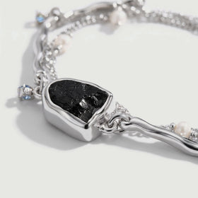 An angled close view reveals the raised silver setting around the rough black stone and its connection to a curved bar.