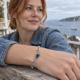 A freckled woman in a blue jacket wears the silver bracelet while resting her wrist on a wooden railing beside the sea.