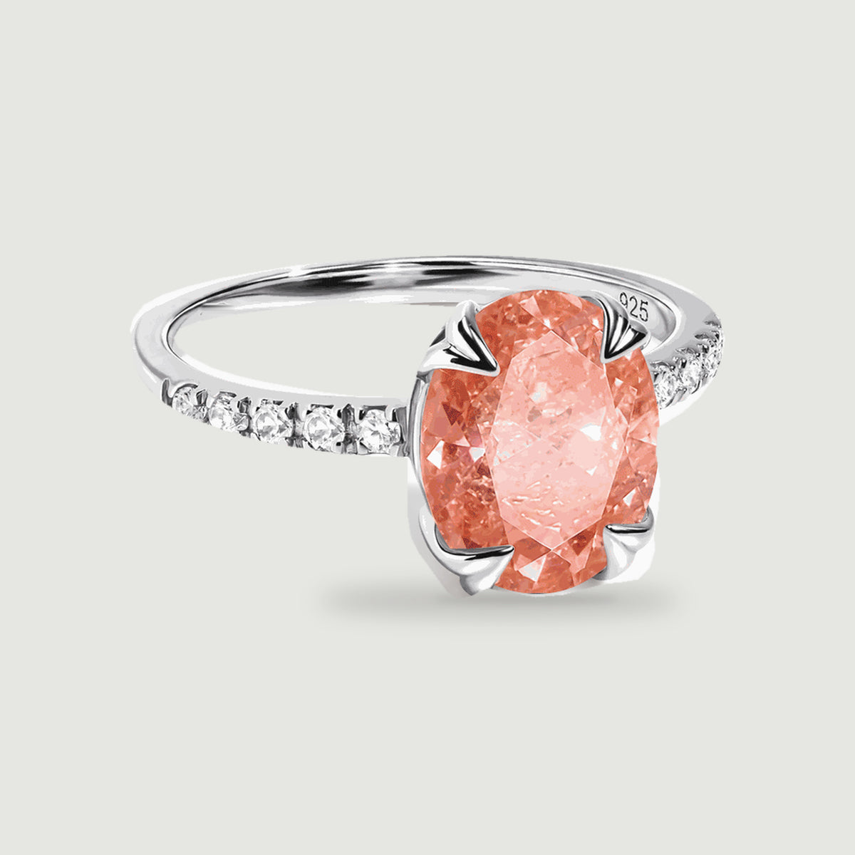 A silver ring with an oval coral peach gemstone and clear stones along the band rests on a light gray background.