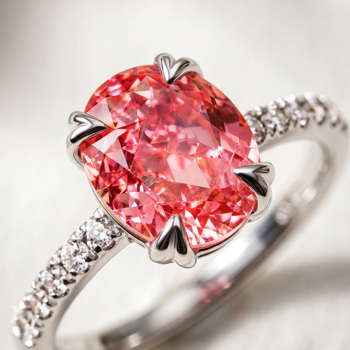 A close view shows the coral pink oval gemstone, polished silver heart-shaped prongs, and clear shoulder stones.