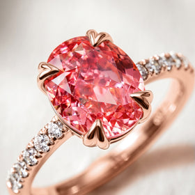 The pink oval gemstone is shown in close detail with rose gold heart-shaped prongs and a slender stone-set band.