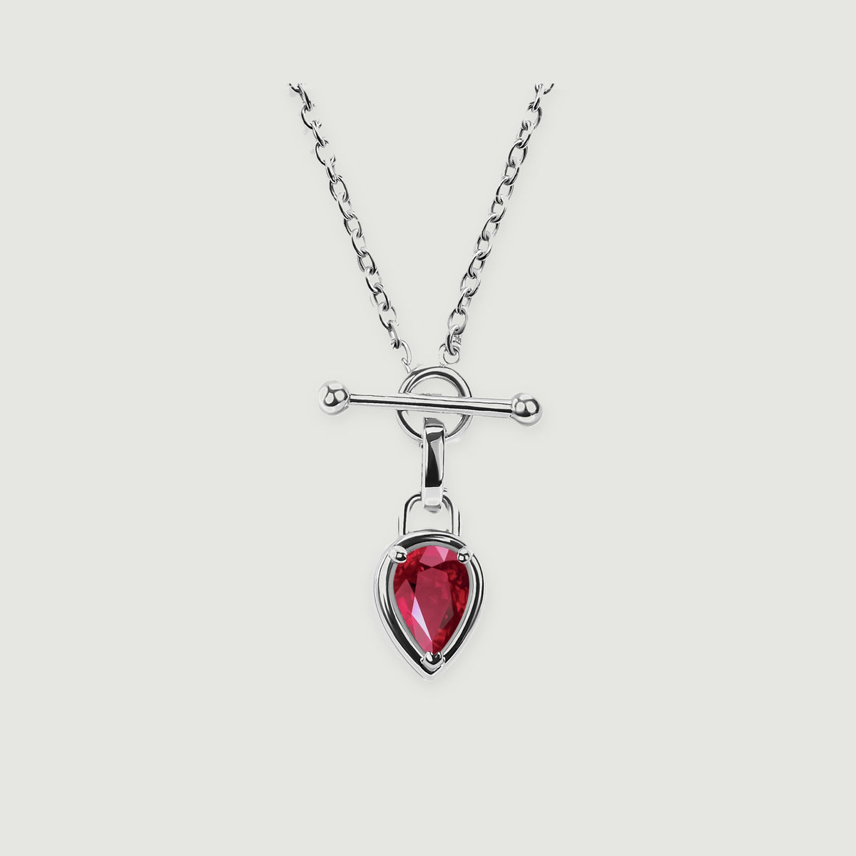 A silver-tone necklace shows a faceted red drop, an open circular clasp, and a smooth horizontal bar against pale gray.