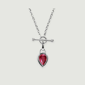 A silver-tone necklace shows a faceted red drop, an open circular clasp, and a smooth horizontal bar against pale gray.