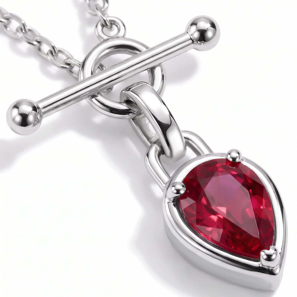 A diagonal silver-tone bar crosses the circular clasp above the red pear-shaped stone in this close view.