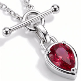 A diagonal silver-tone bar crosses the circular clasp above the red pear-shaped stone in this close view.