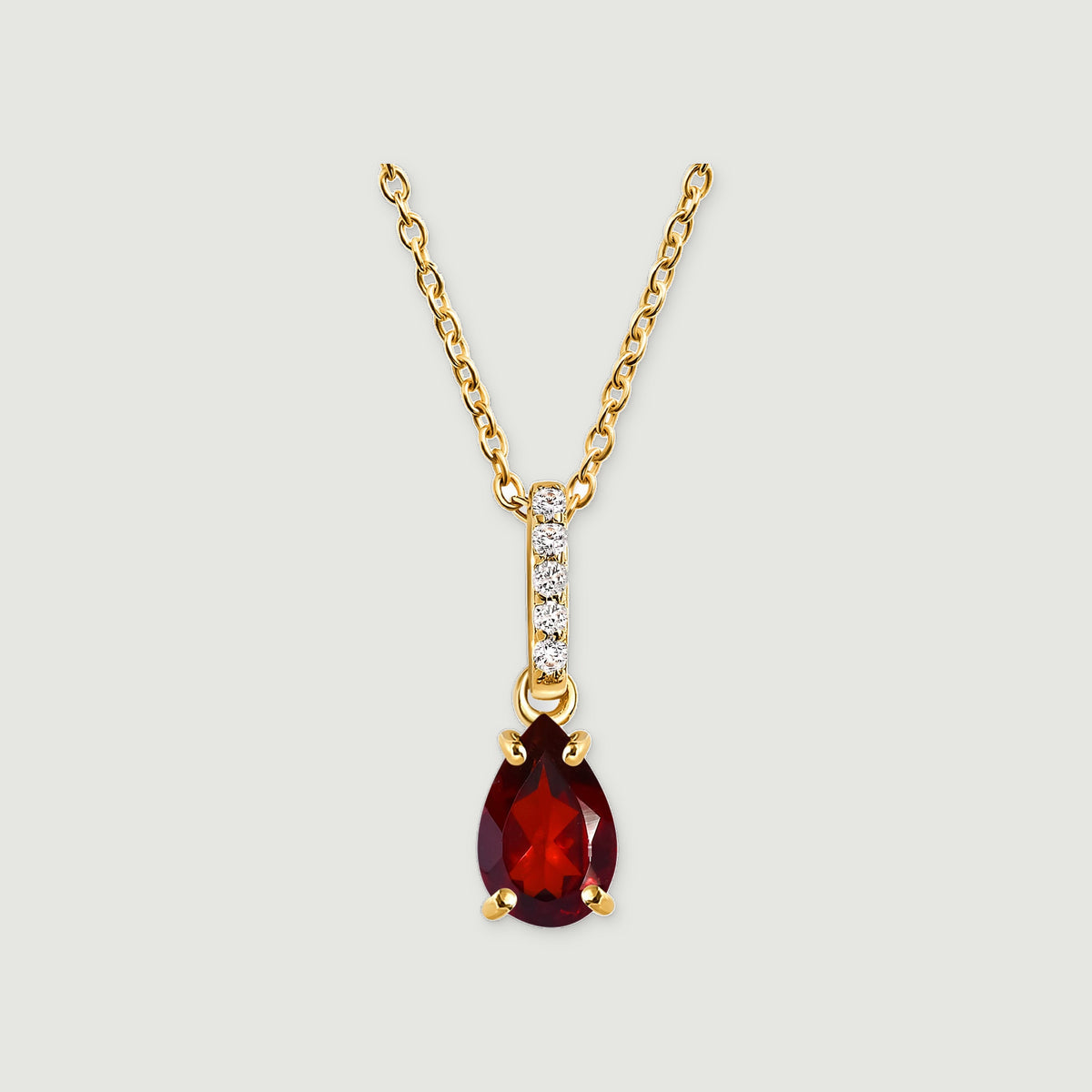 A yellow gold necklace has a pear-shaped deep red gemstone beneath a slim diamond-set bail on a light gray background.