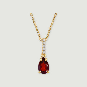A yellow gold necklace has a pear-shaped deep red gemstone beneath a slim diamond-set bail on a light gray background.