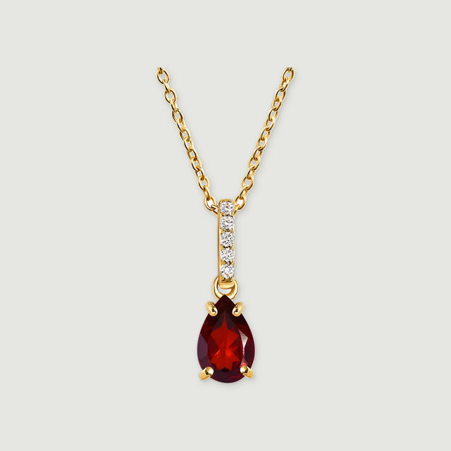 A yellow gold necklace has a pear-shaped deep red gemstone beneath a slim diamond-set bail on a light gray background.