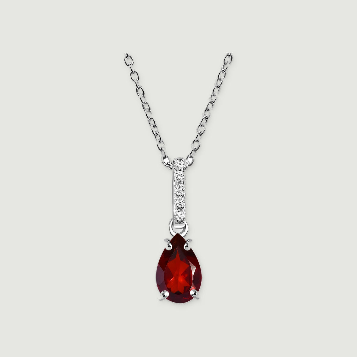 A silver chain holds a red pear-shaped pendant with four prongs and a vertical row of bright stones on light gray.