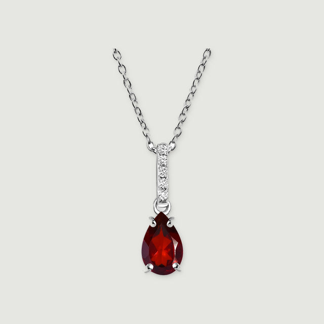 A silver chain holds a red pear-shaped pendant with four prongs and a vertical row of bright stones on light gray.