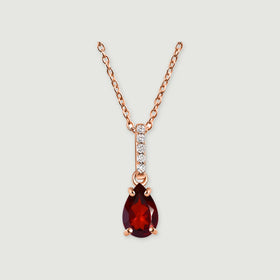 A rose gold necklace displays a faceted red drop and a diamond-set bail against a pale gray surface.