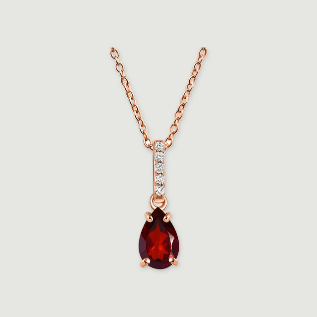 A rose gold necklace displays a faceted red drop and a diamond-set bail against a pale gray surface.