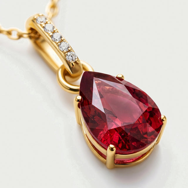 A close view shows the red pear-shaped gemstone, yellow gold prongs and five bright stones along the bail.