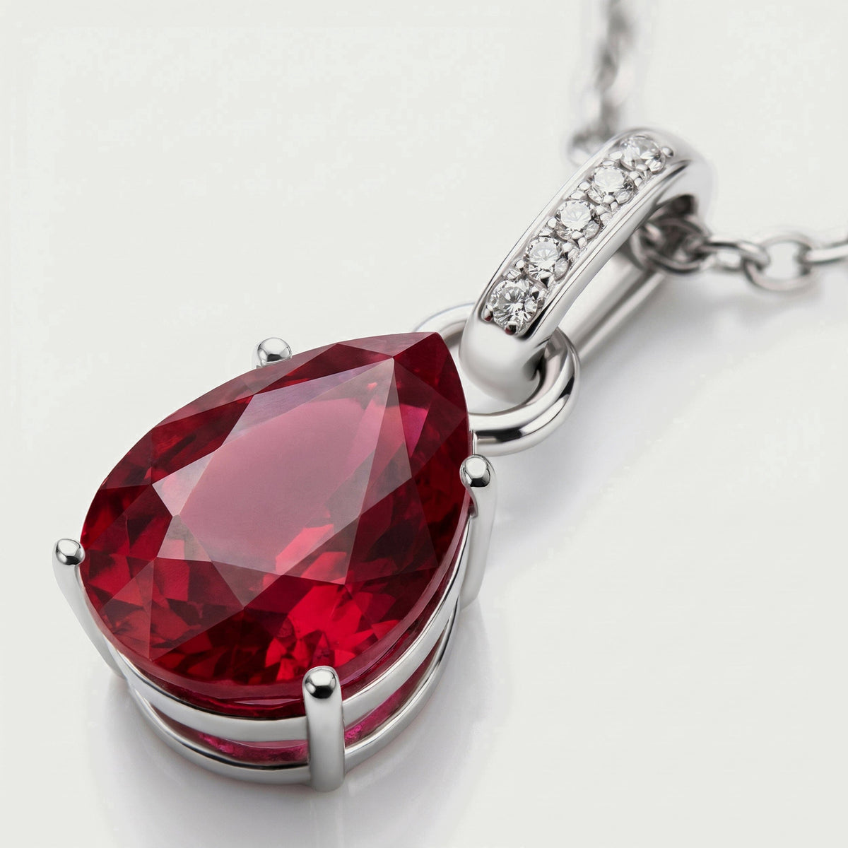 The silver pendant lies diagonally with its red facets, open setting and diamond-set bail visible in close-up.
