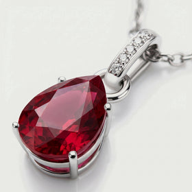 The silver pendant lies diagonally with its red facets, open setting and diamond-set bail visible in close-up.