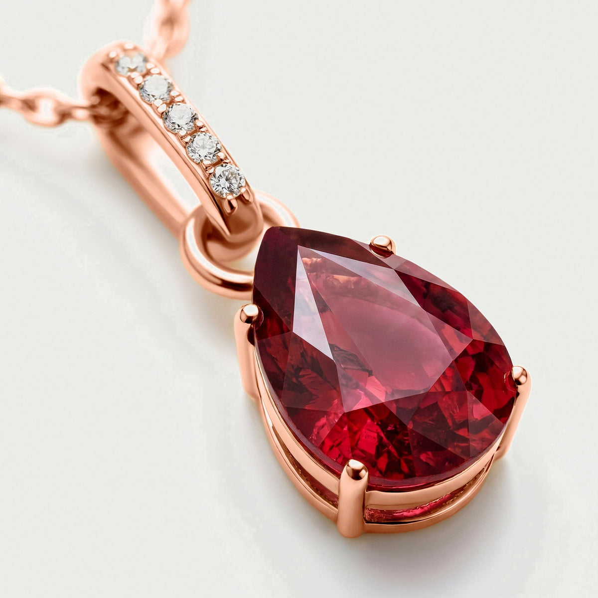 A diagonal close-up reveals warm rose gold prongs around a red drop and the bright stones set into its bail.